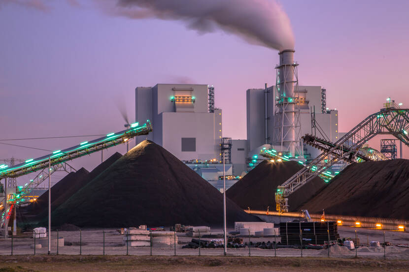 Kolencentrale met rokende schoorsteen en hopen kool op de voorgrond