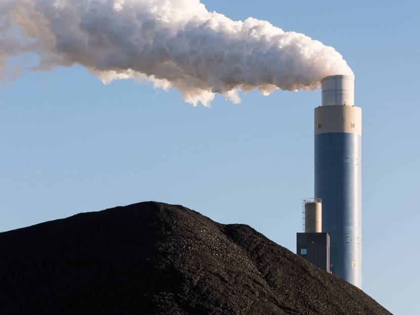 Rokende schoorsteen van een kolencentrale, met berg kolen op de voorgrond.