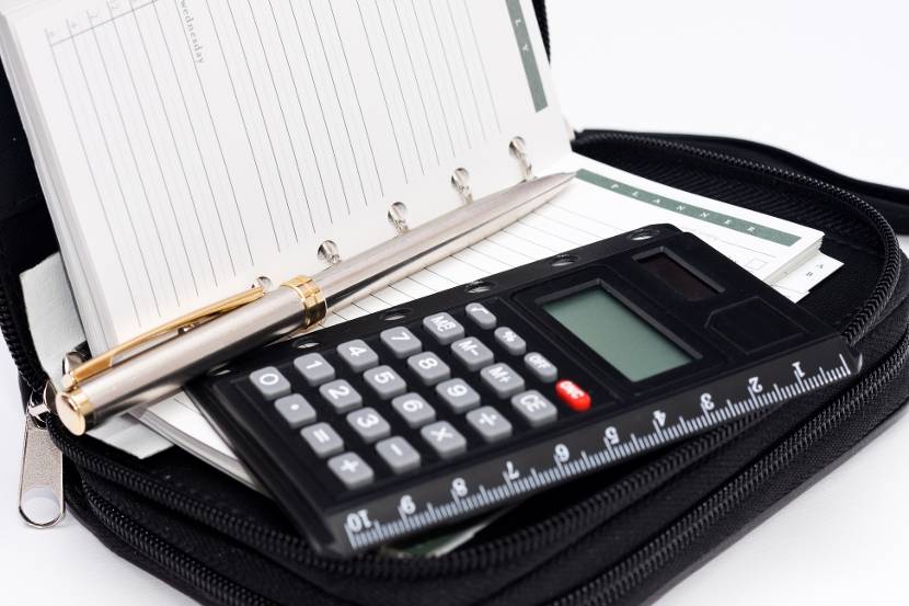 Een zwarte rekenmachine ligt op een open agenda met zilverkleurige pen ernaast.