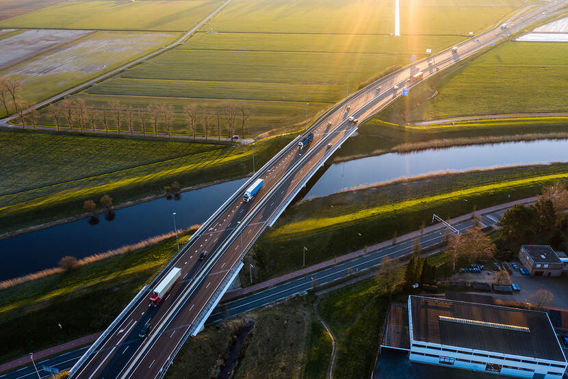 Bovenaanzicht van een autoweg wat door een groen landschap loopt, en over een rivier heen.