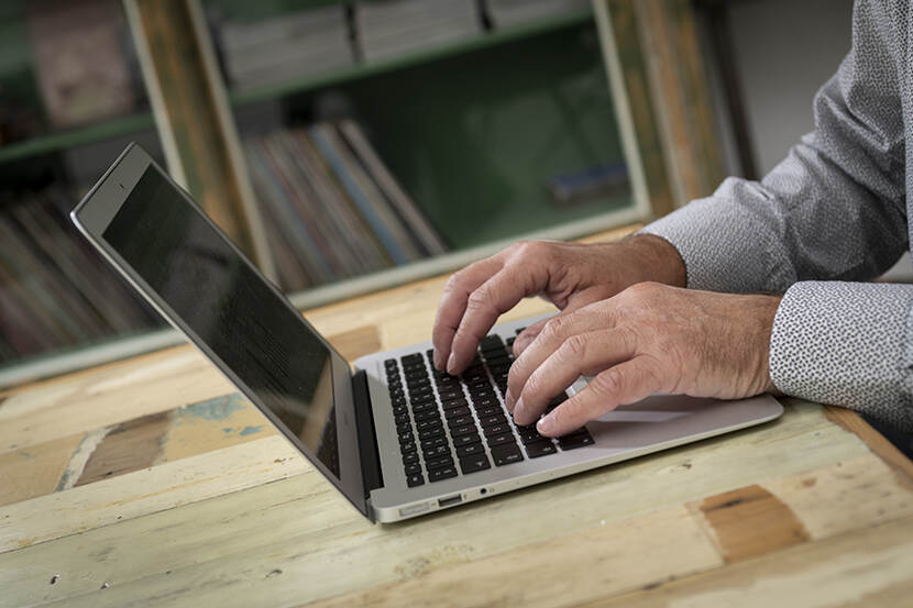 Man achter een laptop met alleen de handen zichtbaar.